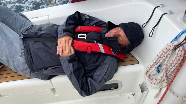 A man wearing jeans and a coat with a red lifejacket sleeping on a boat