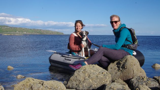 two women wearing lifejackets sitting in a dinghy with their dog