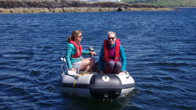 Two women sitting in a dinghy being powered by an outboard motor