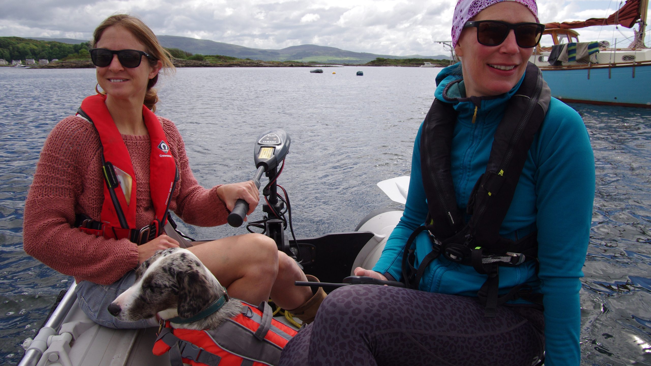 Two women in a dinghy with a dog with a dinghy outboard