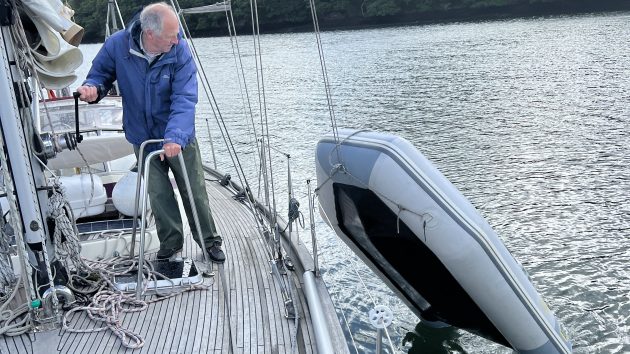 A man lifting a dinghy onto the deck of a yacht