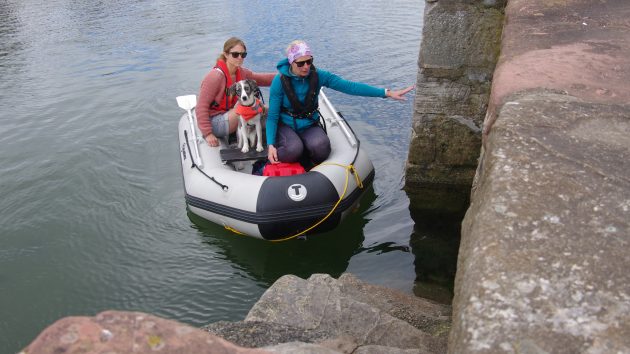Two women and a dog in a lifejaket drifting towards some harbour steps