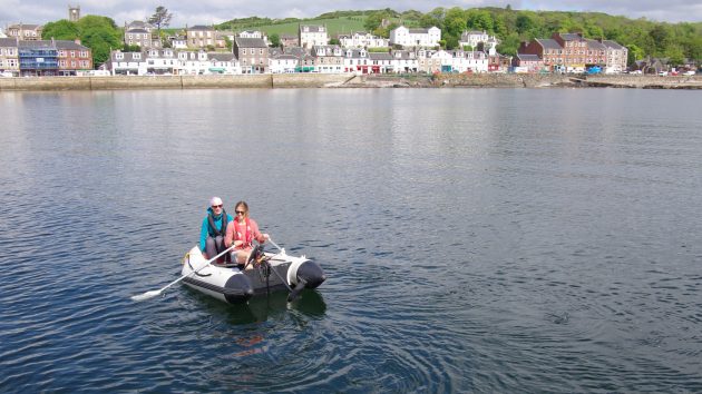 Two women rowing a dinghy in a harbour